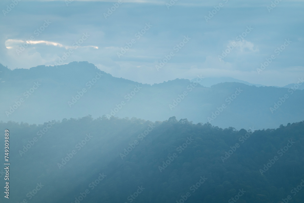 Wall mural sun rays filter through the clouds in hills of the valley illuminated by the sun's rays filtering th