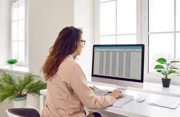Back view portrait of a concentrated young business woman accountant sitting at the desk and...