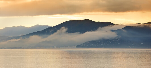 Sea, sunset and fog in clouds with mountains, water and winter season in evening. New Zealand,...
