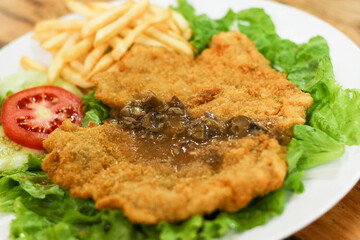 Chicken schnitzel served with mushroom sauce, french fries, lettuce, cucumber and tomato pieces