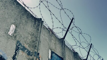 Restricted zone protected with high concrete wall and sharp barbed wire, horror cinematic shot of protected area, concentration camp or military zone, border line control to protect area from illegal