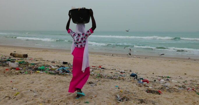 Black African woman dumping rubbish at the edge of the ocean. Appalling plastic pollution. 