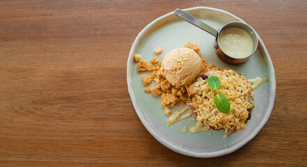 Apple crumble and vanilla ice cream serve with vanilla sauce in white plate on wooden table.