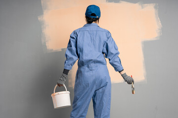 Rear view of painter woman painting the wall with paint brush and bucket. copy space template. wall...