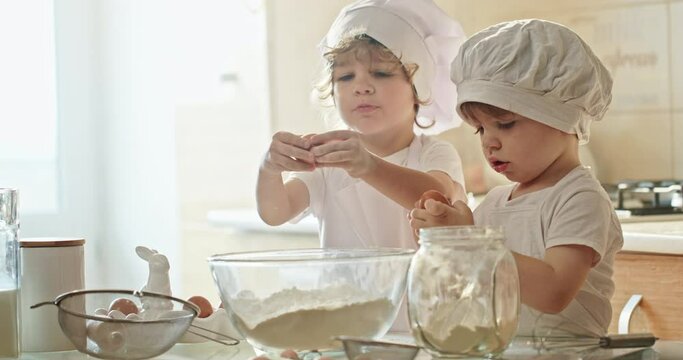 Two toddlers in chef hats are cooking in a kitchen, sharing tableware - Powered by Adobe
