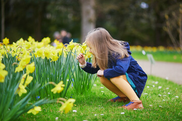 Adorable preschooler girl enjoying nice spring day in park during jonquils blooming season