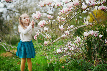 Adorable preschooler girl enjoying nice spring day in park during magnolia blooming season