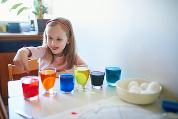 Adorable preschooler girl dyeing Easter eggs at home