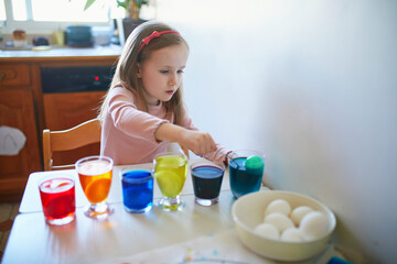 Adorable preschooler girl dyeing Easter eggs at home