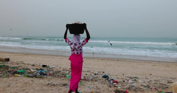 Black African woman dumping rubbish at the edge of the ocean. Appalling plastic pollution. 
