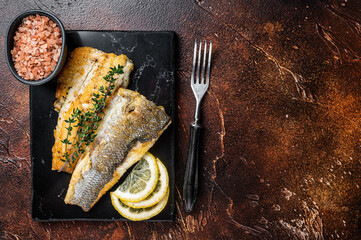 Roast sea bass fillet with lemon and thyme, seabass fish. Dark background. Top view. Copy space