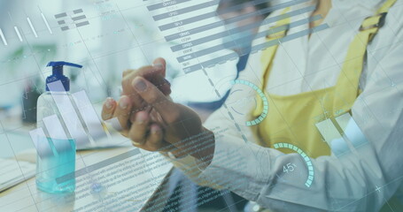 Image of financial data processing over businesswoman disinfecting hands