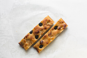 top view of sliced olive and onion focaccia on a white background, Flatlay of focaccia with black olives and red onion topping, fresh homemade focaccia bread on white parchment paper