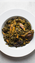 Nigerian vegetable soup with fish and bush meat in a white plate, afang soup in a large dinner plate, traditional edikang ikong soup in a white dish