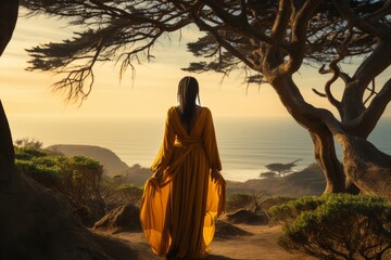 Girl sitting on the top of mounting and enjoying yellow sunrise above sea - obrazy, fototapety, plakaty