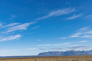 Panoramic view of the Hvannadalshnukur mountain range on the South Coast of Iceland with various glaciers seen from Þjóðvegur or Route 1 with feathered clouds in blue sky