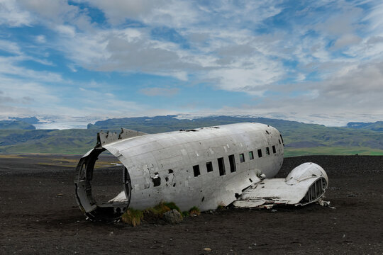 Close up view of demolished and vandalized S&oacute;lheimasandur plane wreck, remains of a 1973 U.S. Navy plane that crashed on the black sand close to Vik, Iceland, with S&oacute;lheimaj&ouml;kull glacier in background
