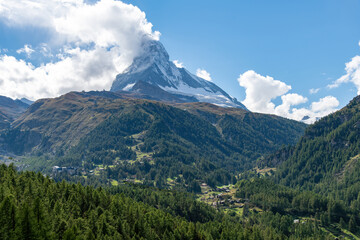 Low angle view of the peak of the Matterhorn partly covered in white clouds in a blue sky and part...