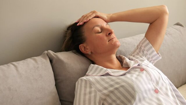 Sadness engulfs exhausted woman lying on sofa holding head in despair She embodies exhaustion reflecting weight of sadness in posture and expression Witness her overwhelming sadness and fatigue