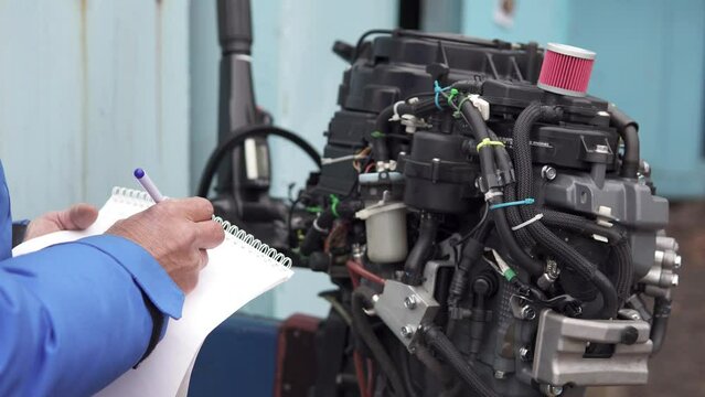 The master writes down in a notebook what parts he needs to buy to repair the outboard motor. Repair of two-stroke and four-stroke injection and carburetor engines.
