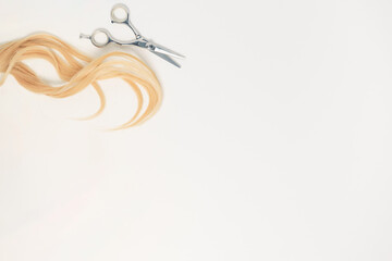 Piece of blonde hair with scissors and copy space on the white background. Hairdresser concept.