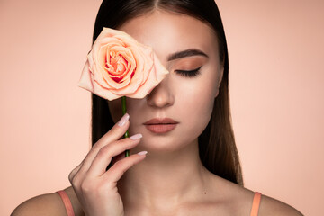 Beauty studio portrait of young beautiful woman holding rose against background in peach tones