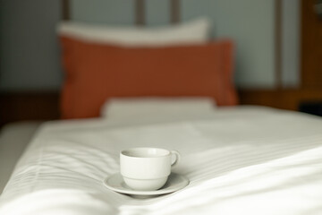 Fototapeta na wymiar Coffee or tea cup on the bed. Hotel room or bedroom Interior, morning time. Concept of easy breakfast. One white ceramic cup.