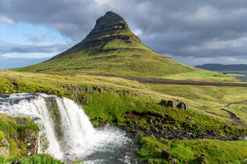 Fototapeta premium Low angle view of the Kirkjufell mountain near Grundarfjordur in Iceland with lower fall of Kirkjufell waterfall in foreground flowing into the sea in background