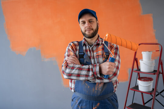 Portrait of a male painter with a paint roller standing against the background of a painted wall in a house with his arms crossed on his chest