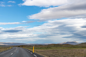 Panoramic view down a curving two lane road on Iceland, through the barren Icelandic Highlands with volcanos and mountains in the northern part of the country with a beautiful blue sky with white fluf