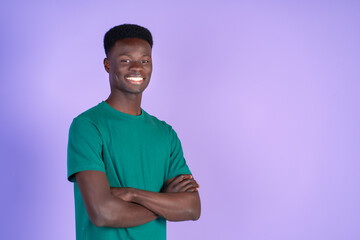 Young smiling black man wearing green t-shirt, arms crossed, isolated on a violet background. with copyspace.