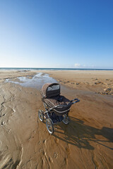 Stroller, sand and blue sky by beach in nature for travel, vacation or holiday in summer. Baby pram, coast and ocean by seashore for tropical weekend trip on outdoor island destination in Cape town.