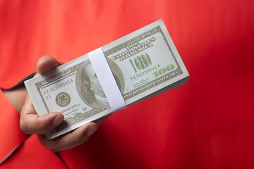 Male hand holding money, hands stretched out from behind a red background.