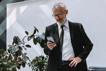Confident mature businessman using smart phone while working in the modern office - 749392057
