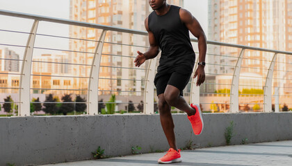 Confident African man in sportswear running outdoors with city skyline on background
