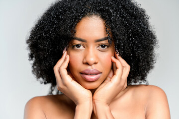 A poised African-American woman with naturally curly hair holds her face gently, her expression...