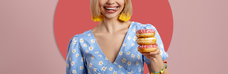 Close-up of playful woman holding doughnuts and sticking out tongue on pink background - 749409637