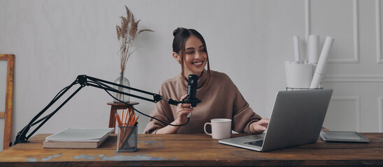 Happy young woman recording podcast while using laptop in studio - 749411257