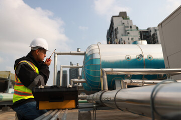 Naklejka premium Industrial engineer wearing green safety jacket holding walkie talkie working about HVAC system
