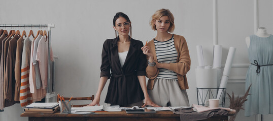 Two confident female fashion designers looking at camera while standing in workshop together - 749414845