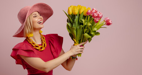 Excited young woman in elegant hat holding bunch of tulips against pink background - 749420868
