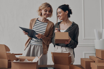 Two happy businesswomen preparing packages for delivery in warehouse together - 749421842