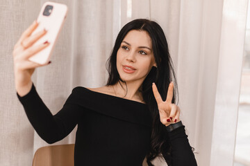 Cafe visitor demonstrating a V-sign to a frontal camera of a mobile phone while taking a picture of...