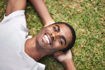 Portrait, smile and relax with black man on grass in garden to enjoy summer or nature outdoor. Face, field and green with happy young person in sunshine alone for peace, calm or quiet from above