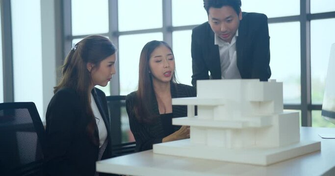 Asian business woman presenting building model with team in office. They dissing about building model design together.