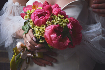 A bride in a white dress with puffy sleeves holds a wedding bouquet of bright pink peonies in her...