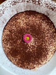 Close up shot from above of a modern restaurant tiramisu dessert with edible flower decoration.