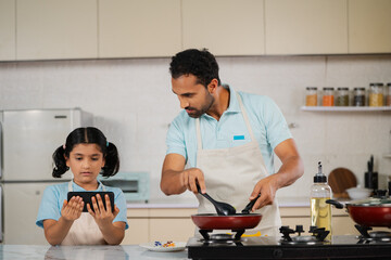 curious father with daughter cooking together by watching online video from mobile phone at kitchen...