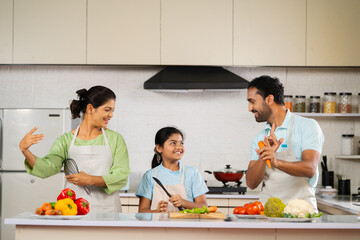 Joyful Indian father mother and kid dancing together at kitchen while cooking during weekend holidays - concept of family bonding, entertainment and lively family.