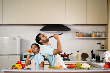 Joyful Indian father with kid dancing together at kitchen while cooking - concept of weekend holidays, family bonding and happy parenting